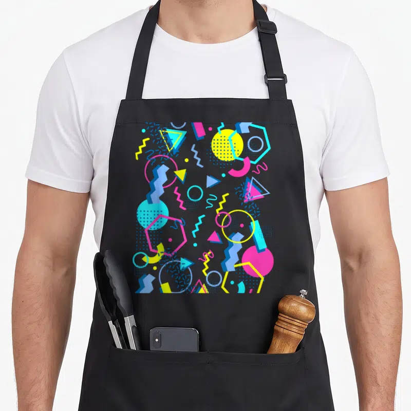 Pattern memphis apron - Scattered geometric shapes in yellow pink blue and cyan on black background — shown on a black cotton canvas apron against a white background