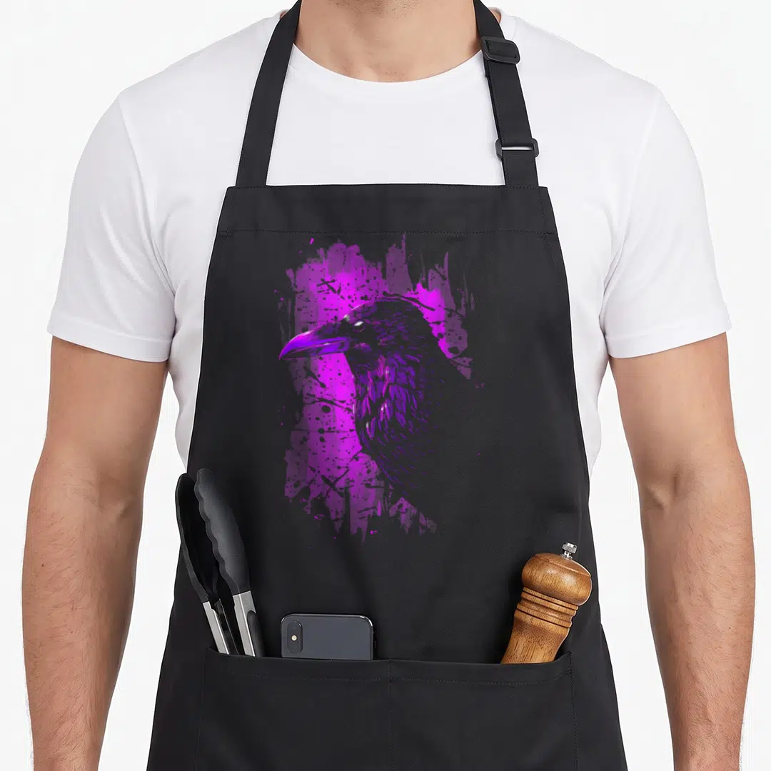 Dye crow apron - Purple line-art crow head profile over abstract paint splashes — shown on a black cotton canvas apron against a white background