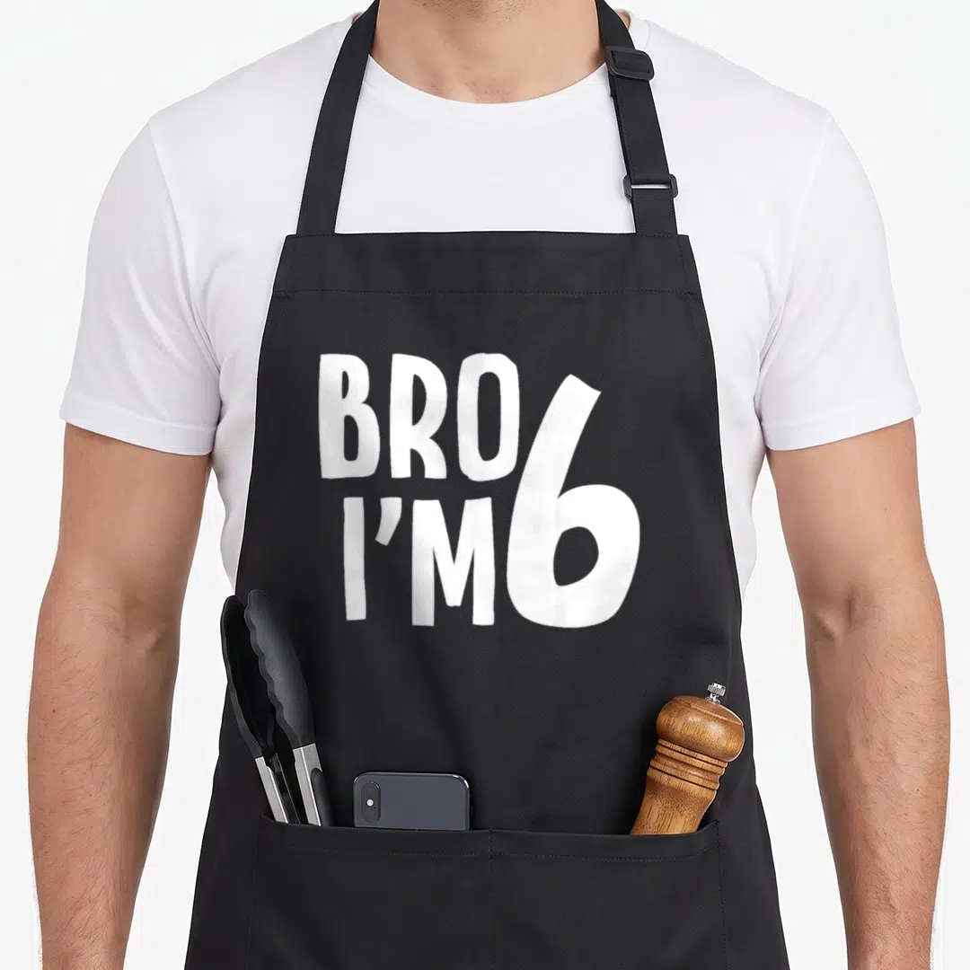 Bro birthday apron - White stacked text BRO I'M 6 typography design — shown on a black cotton canvas apron against a white background