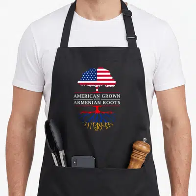 Grown armenian apron - Tree with US flag leaves and Armenian flag roots split by banner reading American Grown — shown on a black cotton canvas apron against a white background