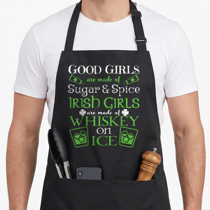 Whiskey funny irish aprons - Good Girls Sugar Spice Irish Girls Whiskey on Ice text with green glasses and shamrocks — shown on a black cotton canvas apron against a white background