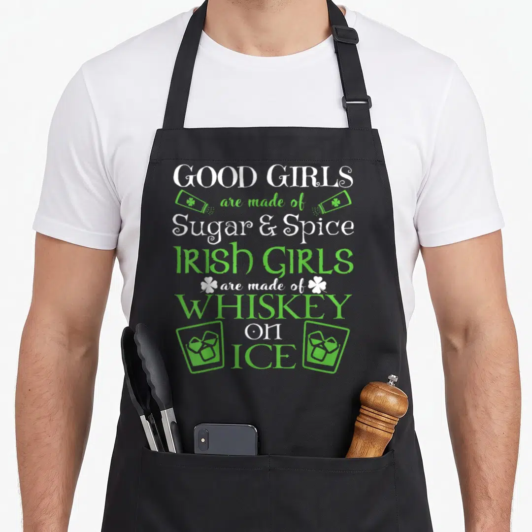 Whiskey funny irish aprons - Good Girls Sugar Spice Irish Girls Whiskey on Ice text with green glasses and shamrocks — shown on a black cotton canvas apron against a white background