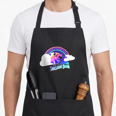 Sunshine rainbow apron - Retro KC and the Sunshine Band logo with rainbow, clouds, and sun graphic in purple, blue — shown on a black cotton canvas apron against a white background