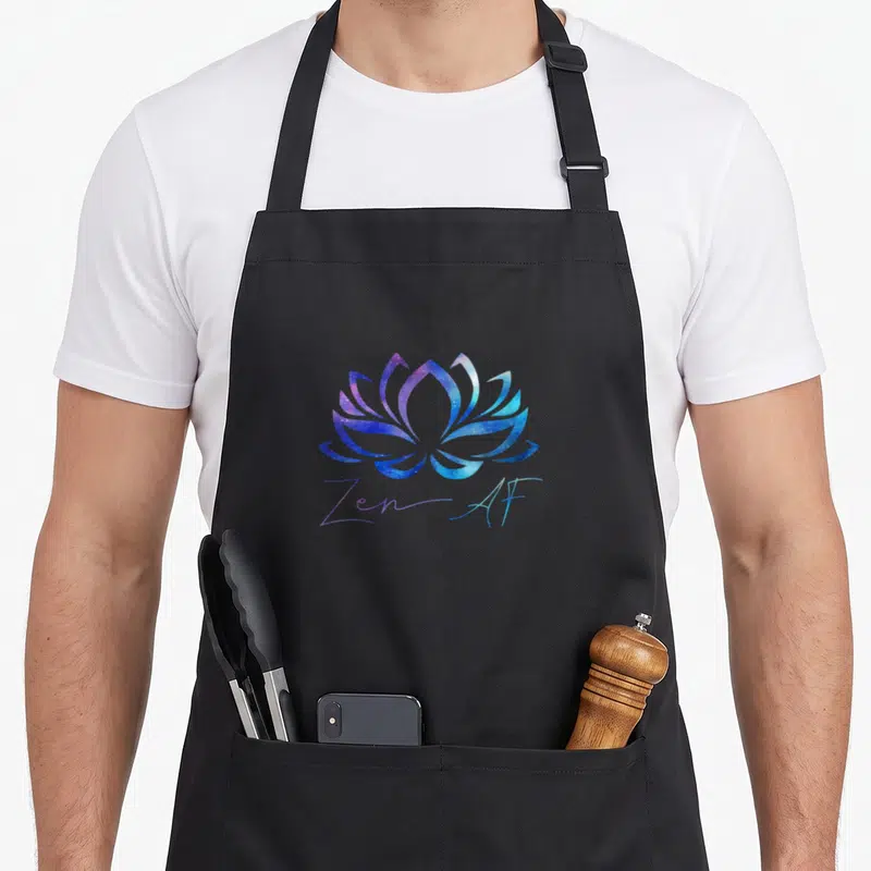 Zen funny passion apron - Galaxy textured lotus flower in purple and blue above handwritten Zen-AF text — shown on a black cotton canvas apron against a white background