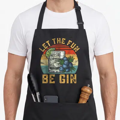 Tonic gin apron - Retro glass of gin with lime, berries, and striped sun background with yellow text — shown on a black cotton canvas apron against a white background