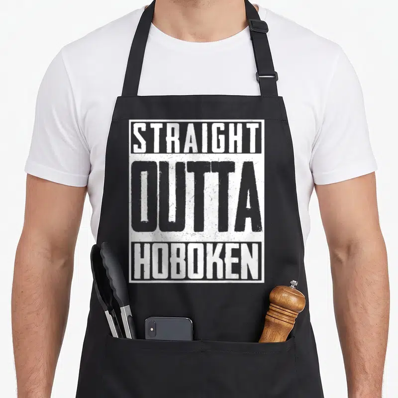 Straight patriots apron - Stacked white and grey text reading STRAIGHT OUTTA HOBOKEN inside a rectangular border — shown on a black cotton canvas apron against a white background