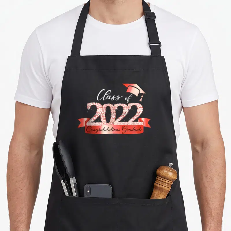 Class congratulation apron - Red and white rhinestone 2022 numbers with graduation cap and red ribbon text — shown on a black cotton canvas apron against a white background