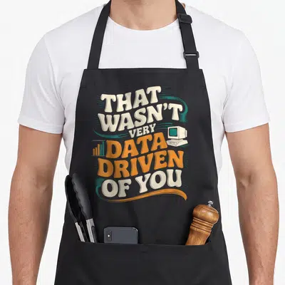 Analyst modern apron - Retro computer and bar chart with stacked text That Wasn't Very Data Driven of You in orange — shown on a black cotton canvas apron against a white background