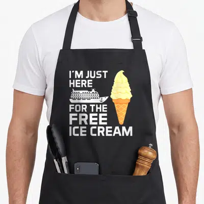 Cruise ice cream apron - Stacked text I'M JUST HERE FOR THE FREE ICE CREAM with white ship and yellow orange cone — shown on a black cotton canvas apron against a white background