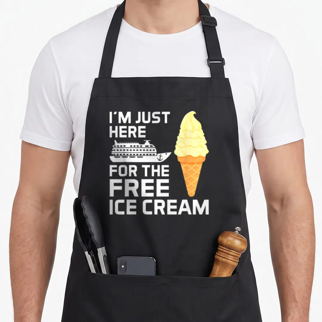 Cruise ice cream apron - Stacked text I'M JUST HERE FOR THE FREE ICE CREAM with white ship and yellow orange cone — shown on a black cotton canvas apron against a white background