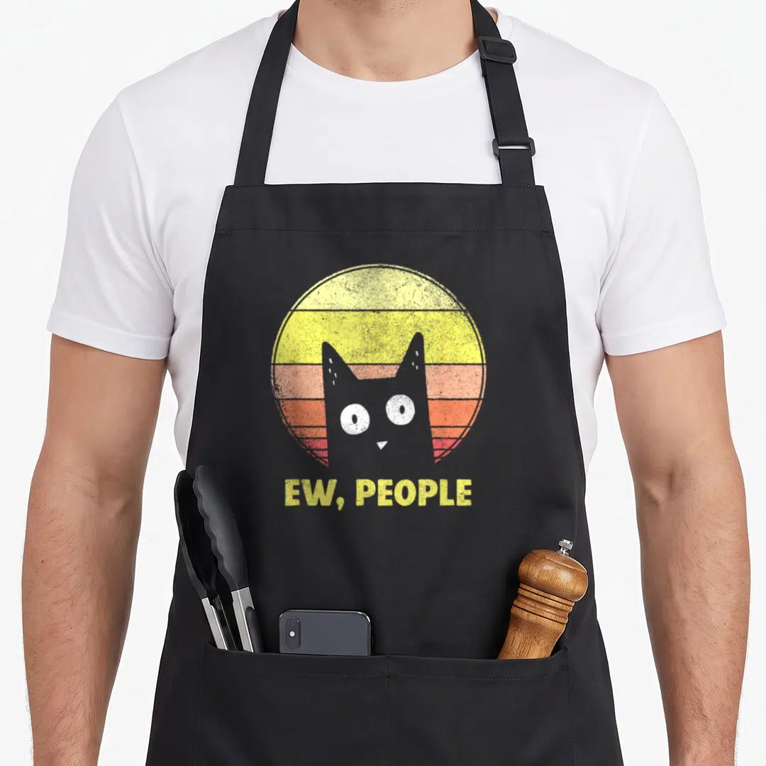 Funny general cat apron for grilling - Grey cat head in front of yellow orange red striped sun with Ew People text below — shown on a black cotton canvas apron against a white background