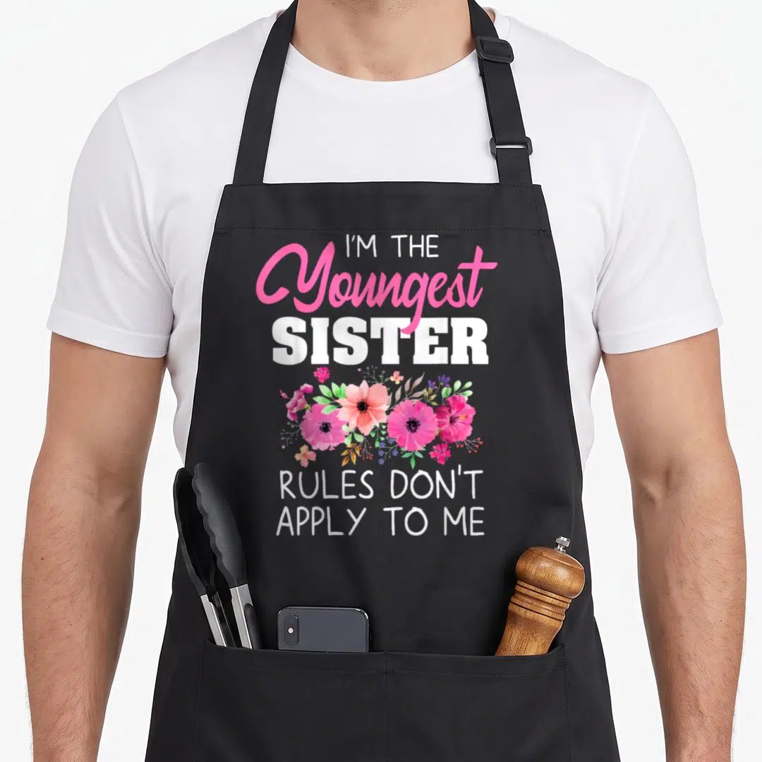 Youngest funny sister apron - Floral watercolor print with text I'M THE Youngest SISTER RULES DON'T APPLY TO ME — shown on a black cotton canvas apron against a white background