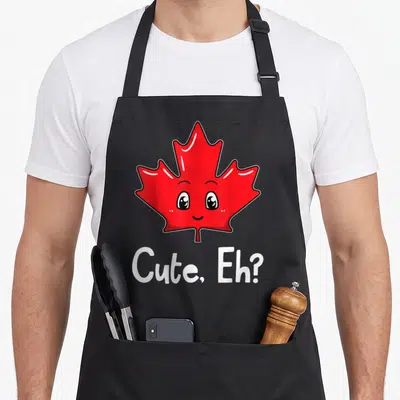 Canada canadian aprons - Red cartoon maple leaf with eyes and smile above white Cute Eh text — shown on a black cotton canvas apron against a white background