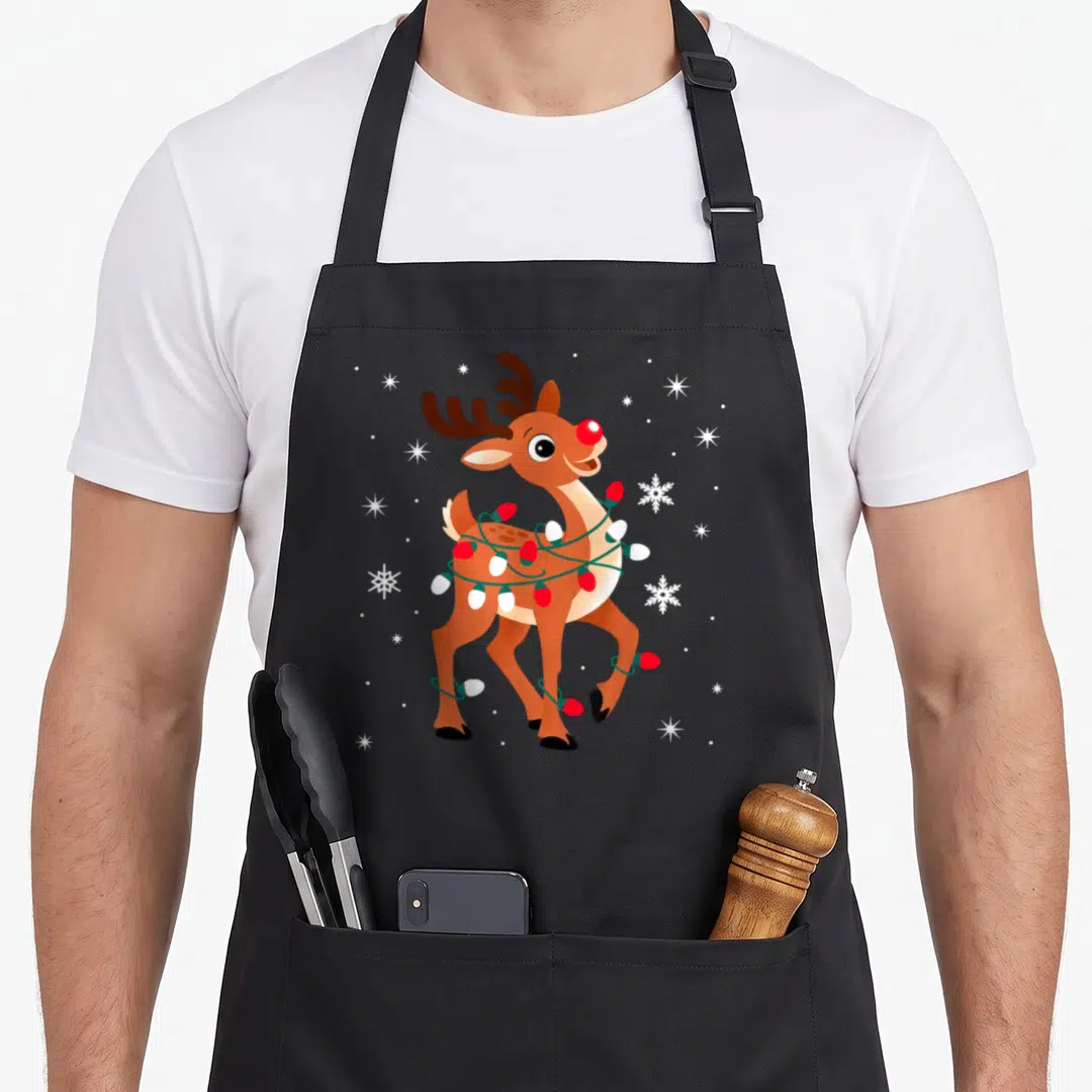 Rudolph nose reindeer red christmas apron - Cartoon reindeer with red nose wrapped in red white and green lights — shown on a black cotton canvas apron against a white background
