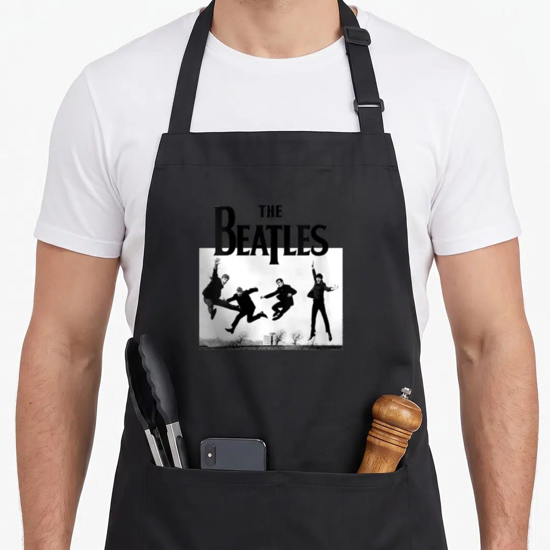 Sefton jump apron - The Beatles text above four men jumping in a black and white photo — shown on a black cotton canvas apron against a white background