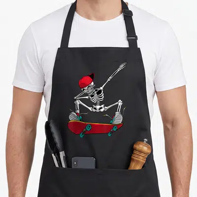 Skateboarding skateboard funny apron - Cartoon skeleton in red cap and shoes standing on red skateboard with teal wheels — shown on a black cotton canvas apron against a white background