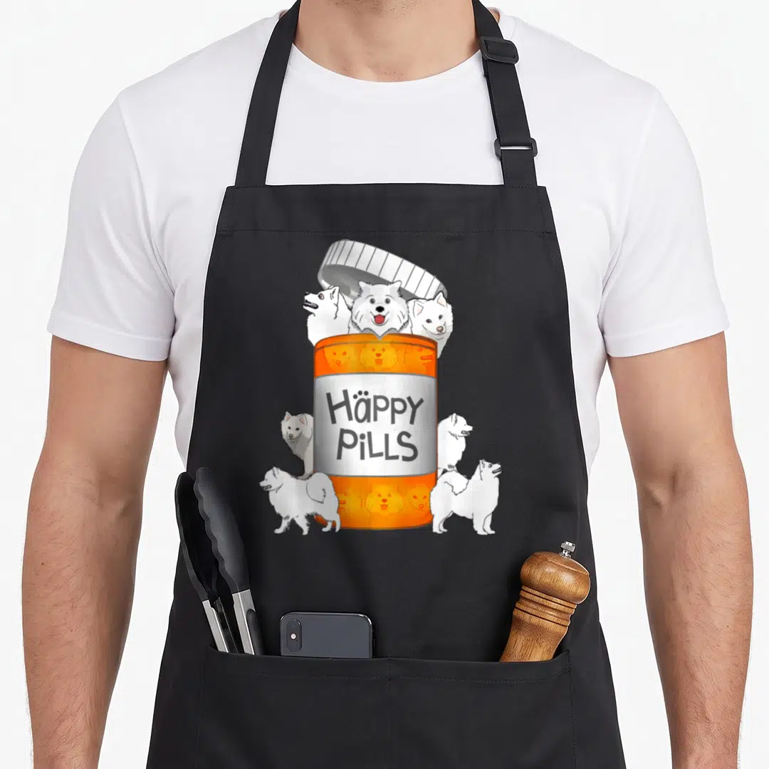 Pill dog apron - Orange pill bottle with six white Samoyed dogs and text Häppy PILLS — shown on a black cotton canvas apron against a white background