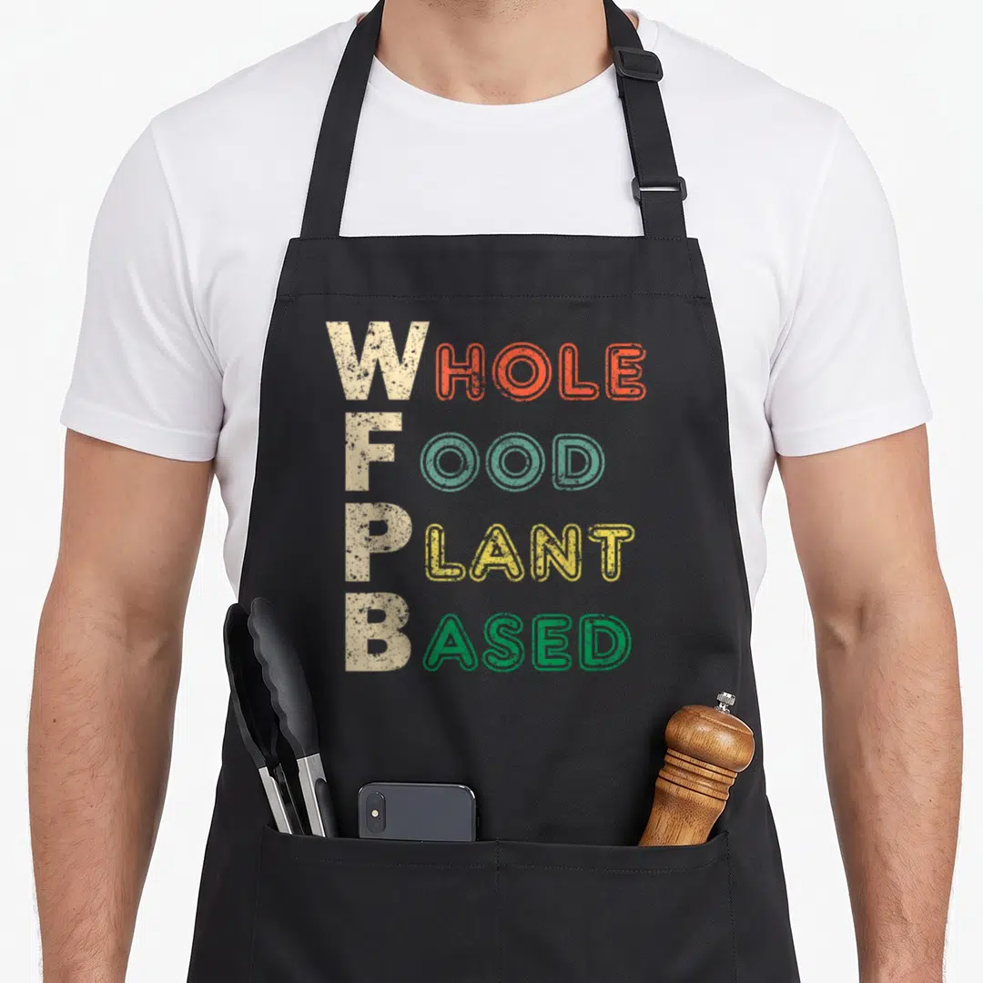 Wfpb whole plant based apron - Stacked W F P B text in orange teal yellow and green with distressed beige letters — shown on a black cotton canvas apron against a white background