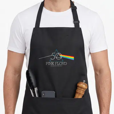 Dark pink floyd apron - Blue prism with rainbow spectrum, 50, PINK FLOYD, THE DARK SIDE OF THE MOON text — shown on a black cotton canvas apron against a white background