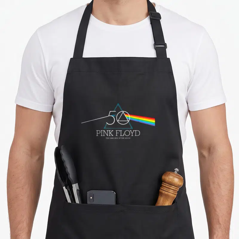 Dark pink floyd apron - Blue prism with rainbow spectrum, 50, PINK FLOYD, THE DARK SIDE OF THE MOON text — shown on a black cotton canvas apron against a white background