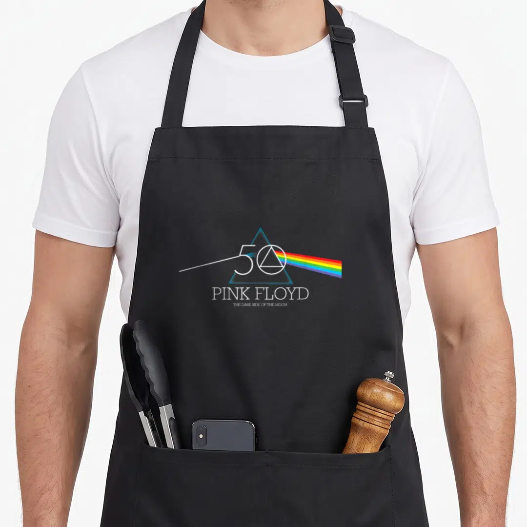 Dark pink floyd apron - Blue prism with rainbow spectrum, 50, PINK FLOYD, THE DARK SIDE OF THE MOON text — shown on a black cotton canvas apron against a white background