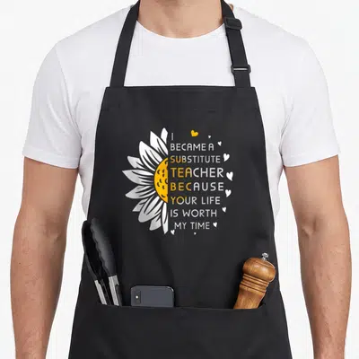 Worth teacher apron - Half sunflower and stacked text I became a substitute teacher because your life is worth my time — shown on a black cotton canvas apron against a white background