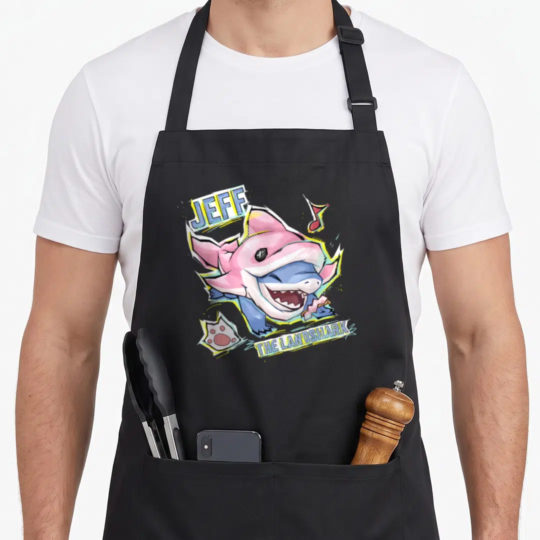 Rival shark apron - Pink and blue cartoon shark labeled Jeff The Landshark with musical note and paw print — shown on a black cotton canvas apron against a white background