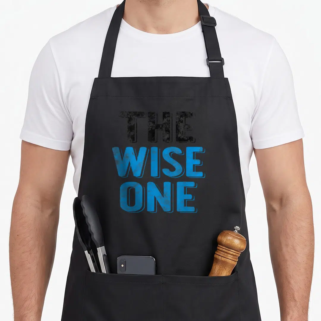 Holiday passover apron - Stacked blue and dark grey text reading THE WISE ONE — shown on a black cotton canvas apron against a white background