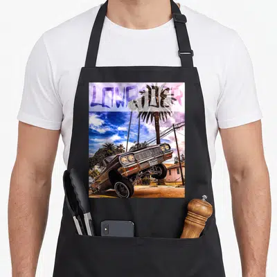 Sunset lowrider apron - Lifted car photo with LOWRIDER text in purple blue over palm trees and house — shown on a black cotton canvas apron against a white background