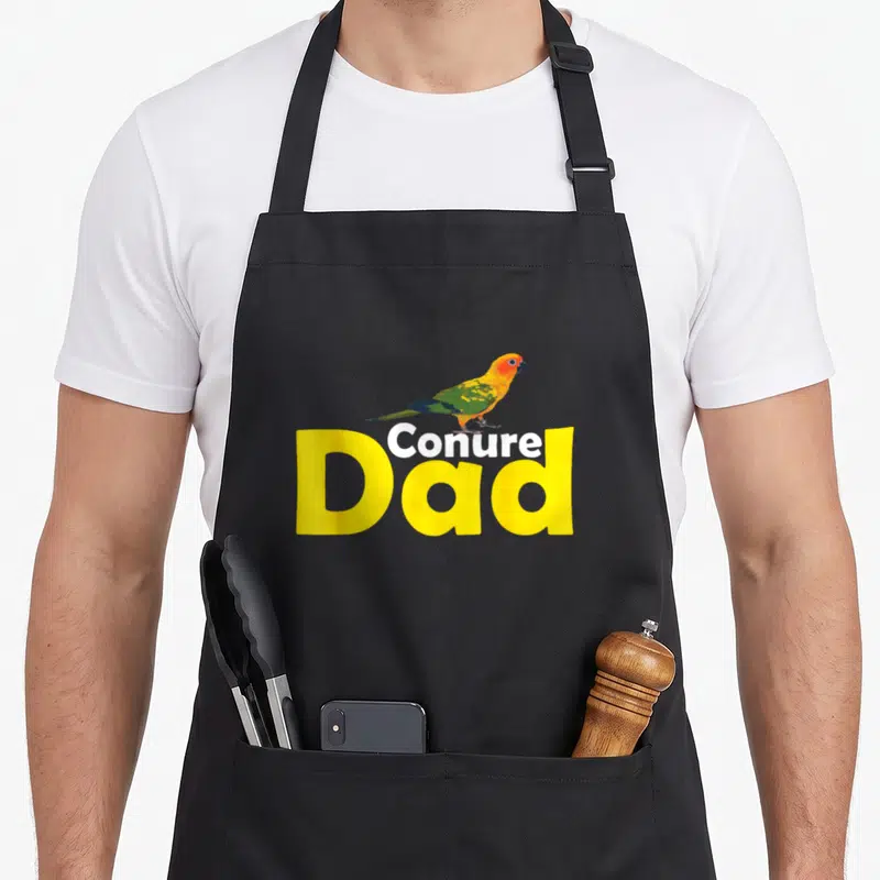 Proud parrot lover apron - Cartoon conure perched on yellow Conure Dad text — shown on a black cotton canvas apron against a white background