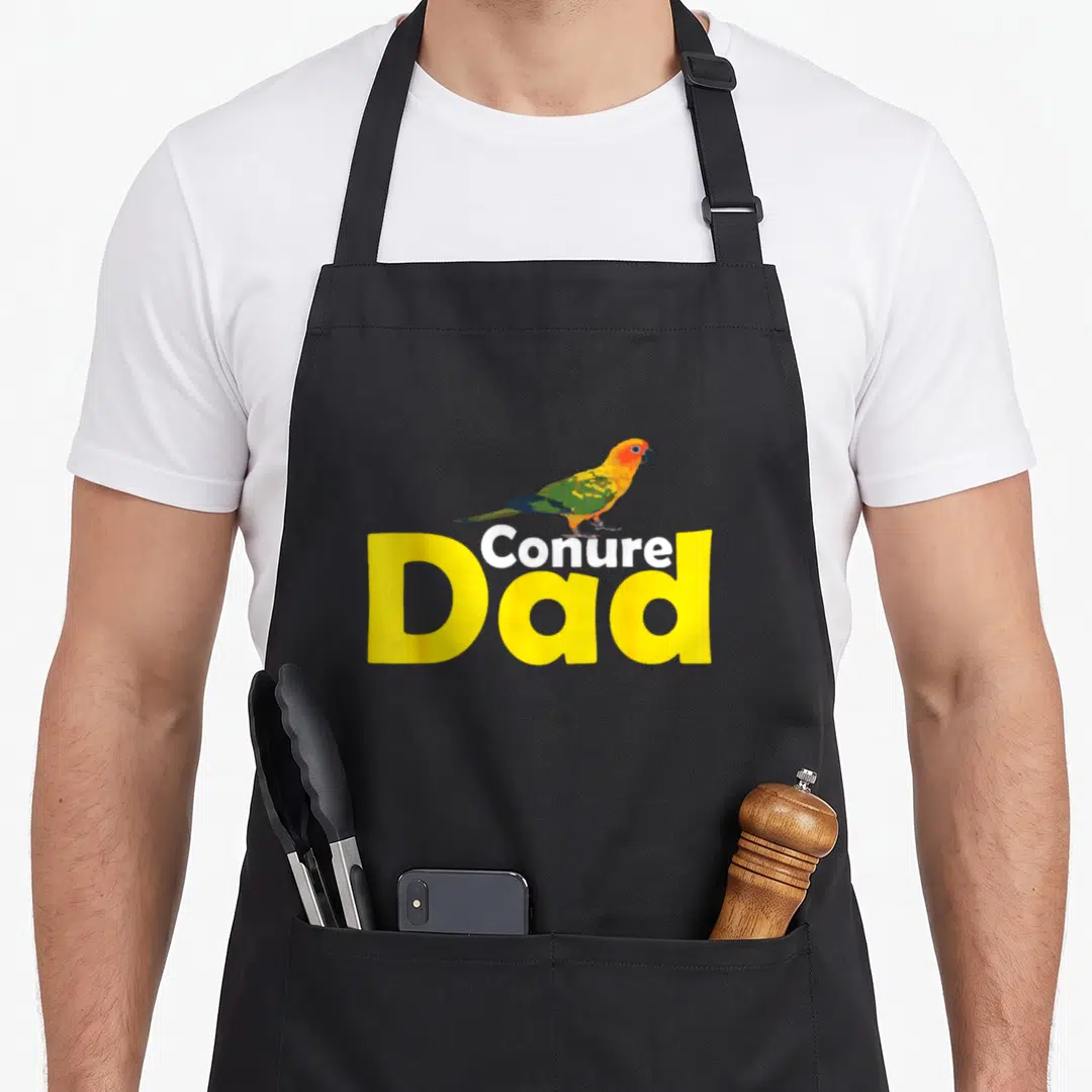 Proud parrot lover apron - Cartoon conure perched on yellow Conure Dad text — shown on a black cotton canvas apron against a white background