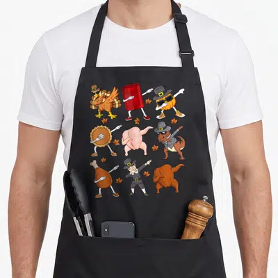 Dabbing pilgrim apron - Cartoon turkey, pumpkin, pie, T-Rex, and pilgrim dabbing in a 3x3 grid with scattered autumn — shown on a black cotton canvas apron against a white background