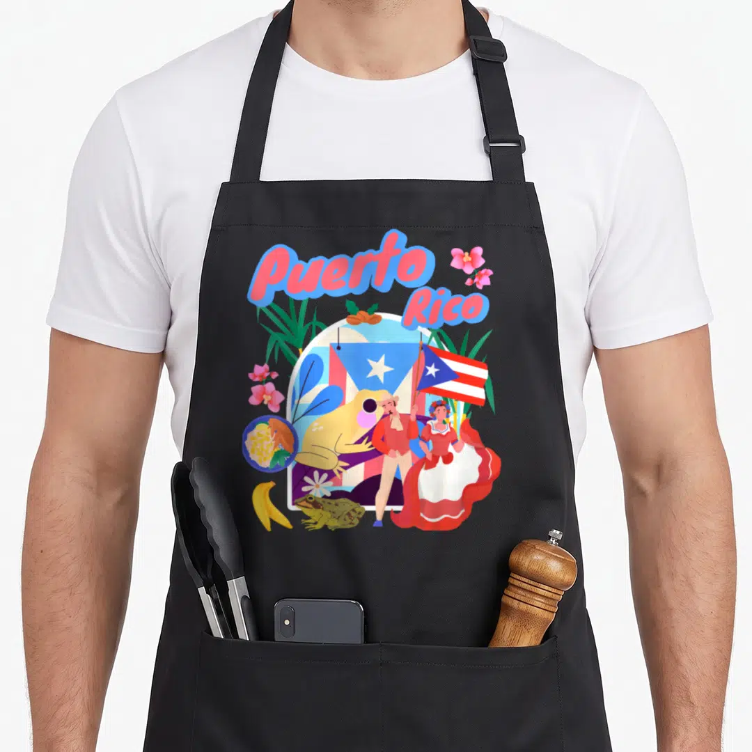 Rican chef outfit with apron - Puerto Rico text over flag, yellow frog, traditional dancers, bananas, and pink flowers — shown on a black cotton canvas apron against a white background