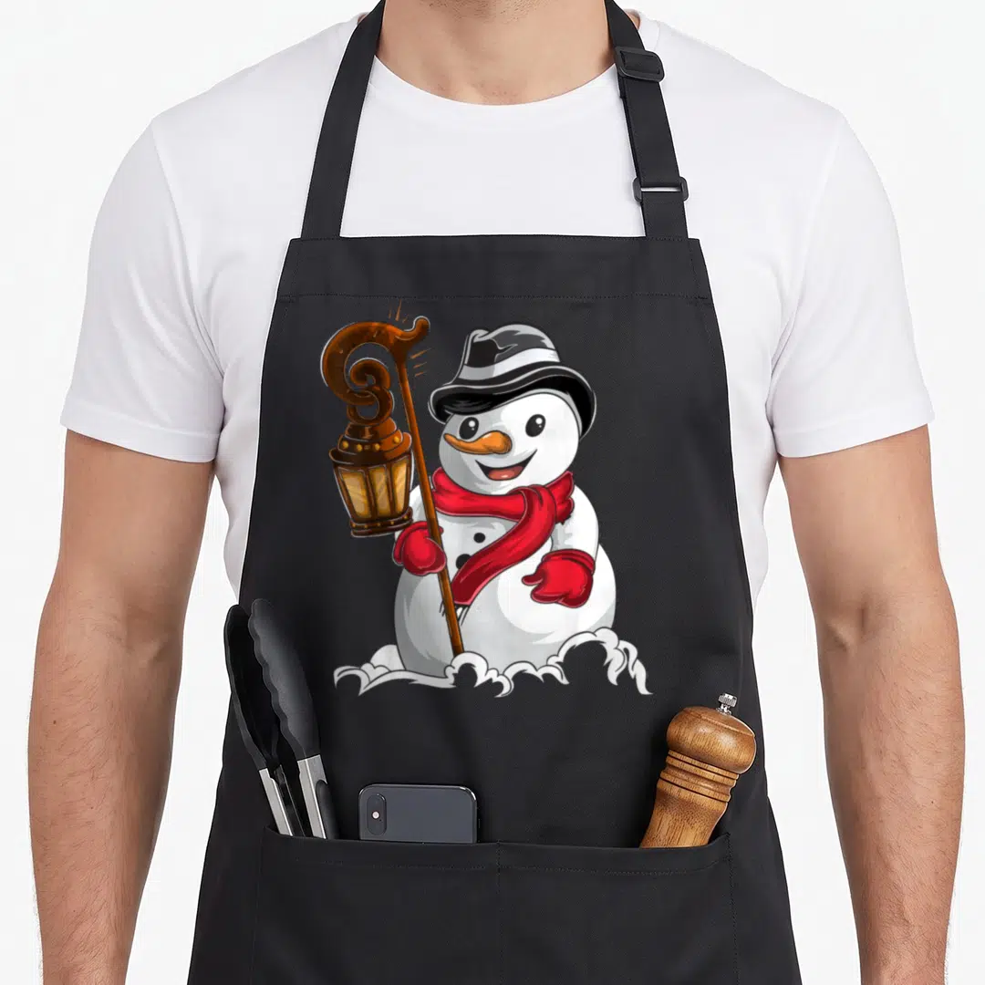 Winter snowman apron - Cartoon snowman holding a brown lantern staff wearing a red scarf and black hat in snow — shown on a black cotton canvas apron against a white background