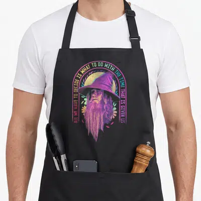 Gandalf ring apron - Retro purple Gandalf portrait inside pink circle with yellow arching quote text — shown on a black cotton canvas apron against a white background