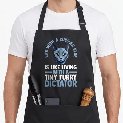 Funny cat russian aprons - Cartoon Russian Blue cat head with arched text and stacked slogan reading tiny furry dictator — shown on a black cotton canvas apron against a white background