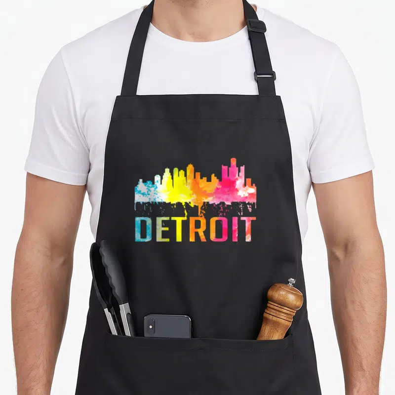 Watercolor detroit apron - Colorful watercolor Detroit skyline and text in blue yellow orange pink gradient — shown on a black cotton canvas apron against a white background