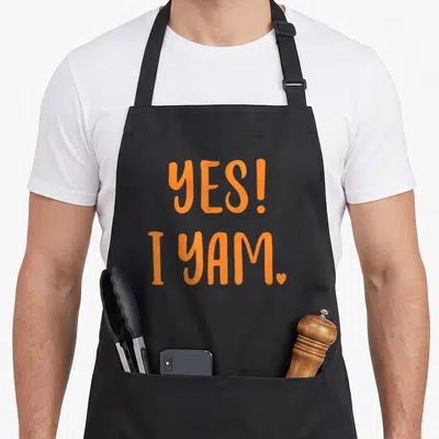 Yam sweet potato apron - Orange text YES! I YAM with a small heart symbol next to the period — shown on a black cotton canvas apron against a white background