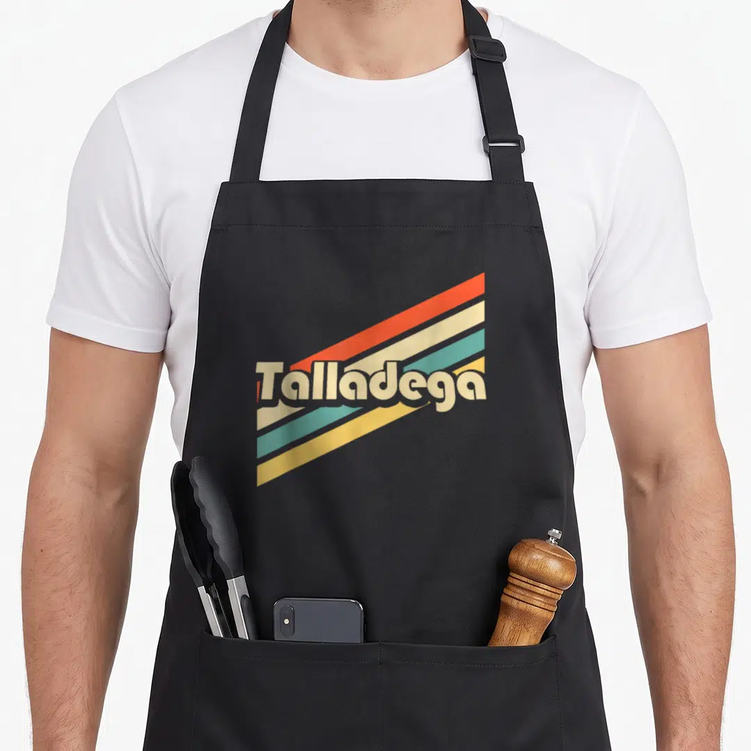 80s alabama apron - Retro Talladega text over four diagonal stripes in orange cream teal and yellow — shown on a black cotton canvas apron against a white background