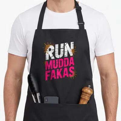Run mud apron - Stacked RUN MUDDA FAKAS text in white and pink with brown splat graphics — shown on a black cotton canvas apron against a white background