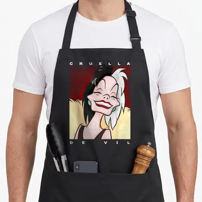 Cruella dalmatian apron - Cartoon Cruella de Vil portrait with spaced CRUELLA DEVIL text on red and yellow background — shown on a black cotton canvas apron against a white background