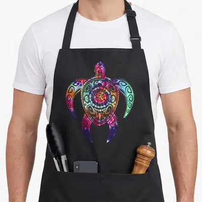 Hippie tie-dye apron - Multicolored sea turtle with tribal lines in pink blue orange green purple watercolor style — shown on a black cotton canvas apron against a white background