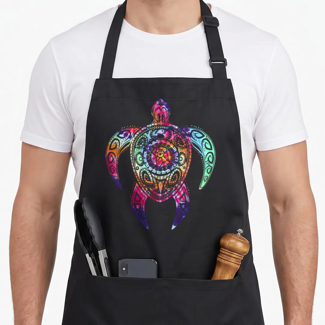 Hippie tie-dye apron - Multicolored sea turtle with tribal lines in pink blue orange green purple watercolor style — shown on a black cotton canvas apron against a white background