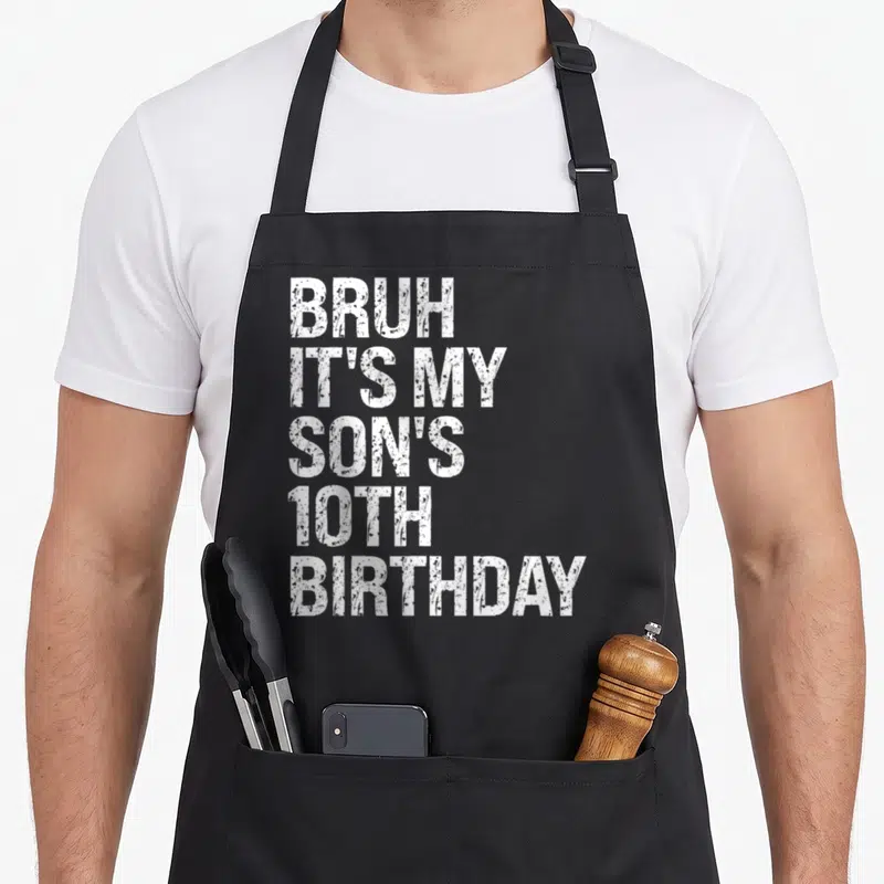 Bruh son birthday apron - White stacked text reading BRUH IT'S MY SON'S 10TH BIRTHDAY on black fabric — shown on a black cotton canvas apron against a white background