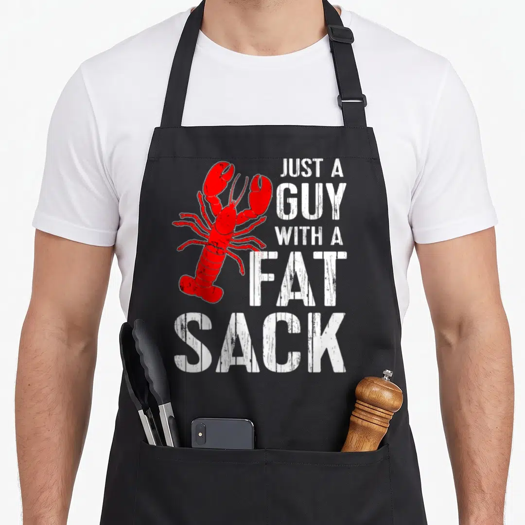 Crawfish fat man in apron - Red lobster illustration next to stacked white distressed text reading JUST A GUY — shown on a black cotton canvas apron against a white background