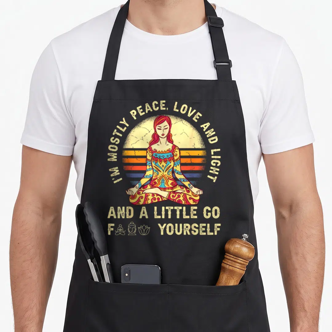 Mostly i love pilates apron - Retro woman meditating before striped sun with sarcastic peace love light text and small — shown on a black cotton canvas apron against a white background