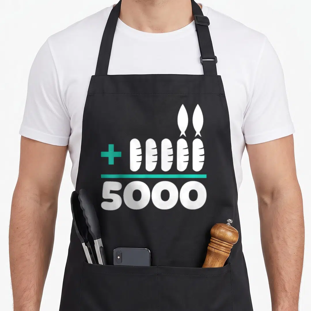 Jesus bread apron - White loaves and fish with teal plus sign and 5000 text — shown on a black cotton canvas apron against a white background