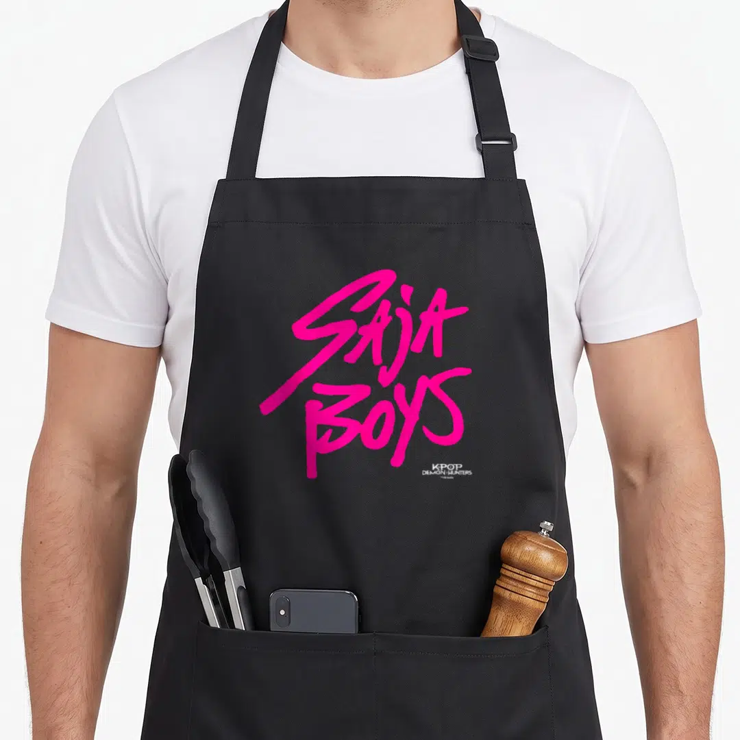 Funny saja trend apron - Pink SAJA BOYS stacked script text with small Kpop Demon Hunters logo watermark — shown on a black cotton canvas apron against a white background