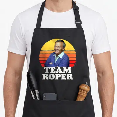 Helen mrs apron - Man portrait in front of yellow orange red striped sun with TEAM ROPER text below — shown on a black cotton canvas apron against a white background