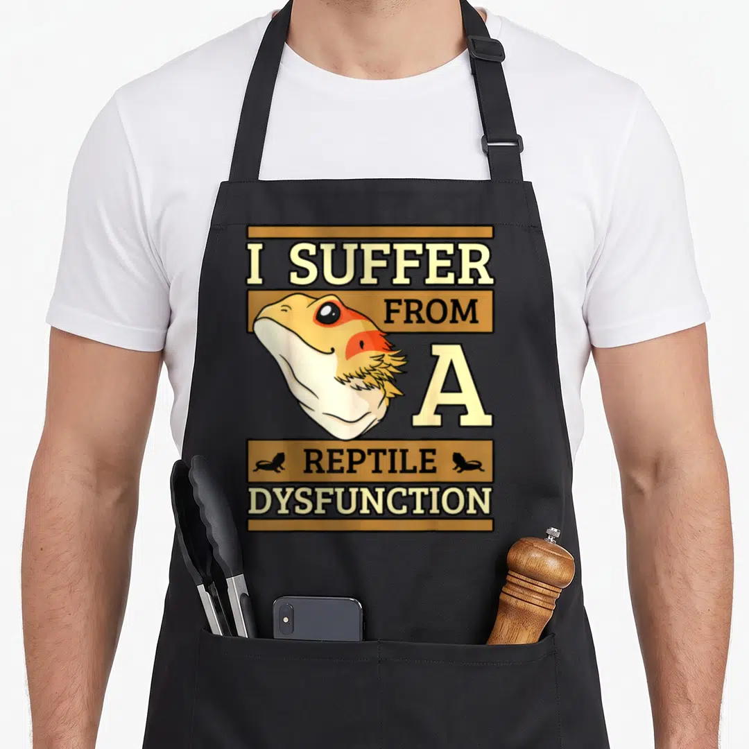 Suffer beard apron - I SUFFER FROM A REPTILE DYSFUNCTION text with bearded dragon head and two lizard silhouettes — shown on a black cotton canvas apron against a white background